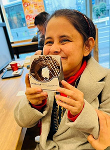 A smiling Mitu-san enjoying a chocolate doughnut on Reflection and Appreciation Day.