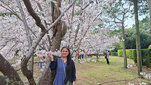 Mitu-san smiling under a cherry blossom tree.