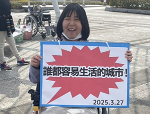 A smiling Coco-san taking part in advocacy activities with a Chinese-language panel at the Center for Independent Living Honya-ra.