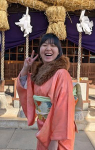 Coco-san in a pink kimono during her New Year homestay, beaming with a bright smile and making a peace sign.