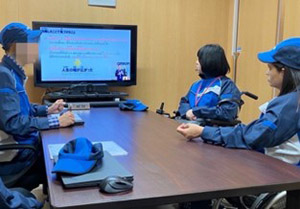 Training at OMRON. Wearing a work uniform, Laxmi-san listens attentively to the staff member's explanation.